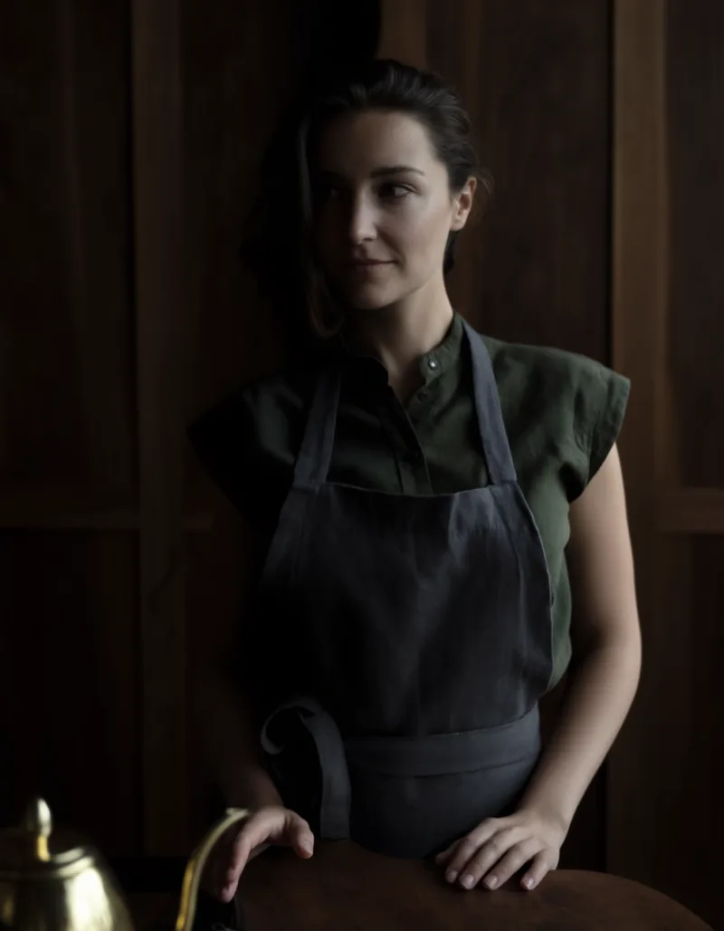 The head barista in a dark linen apron standing behind the walnut bar