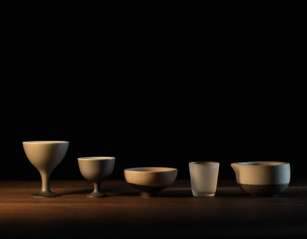 Five plain empty cups in a row on a dark walnut bar, lit from one side