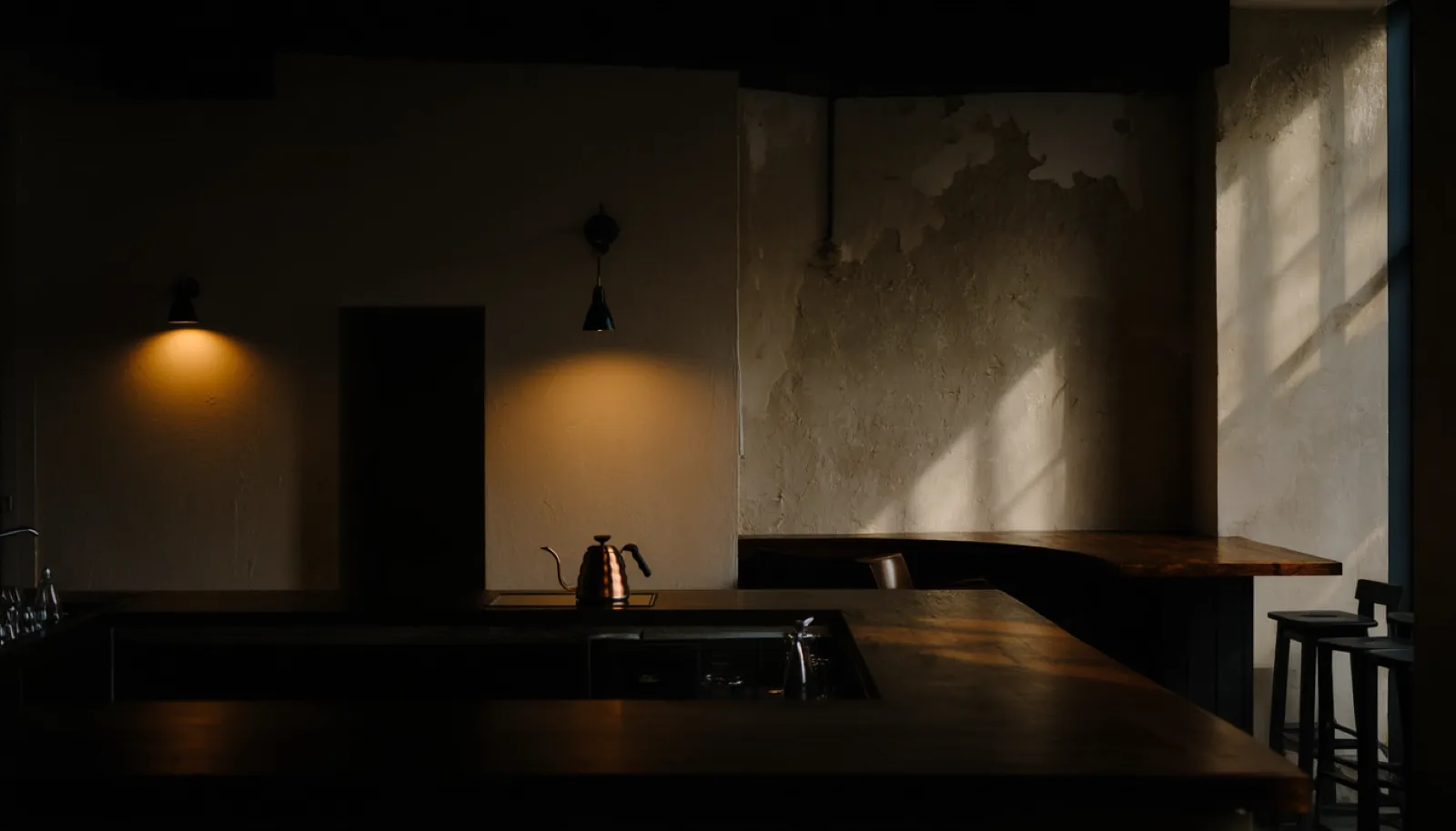 The salon at dusk: a long walnut counter, a brass kettle and low pendant lights